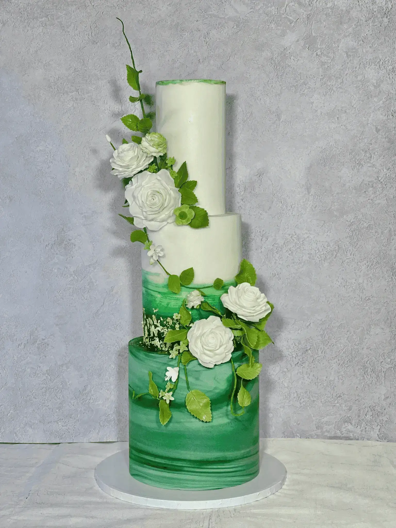 Tall green and white wedding cake with cascading flowers